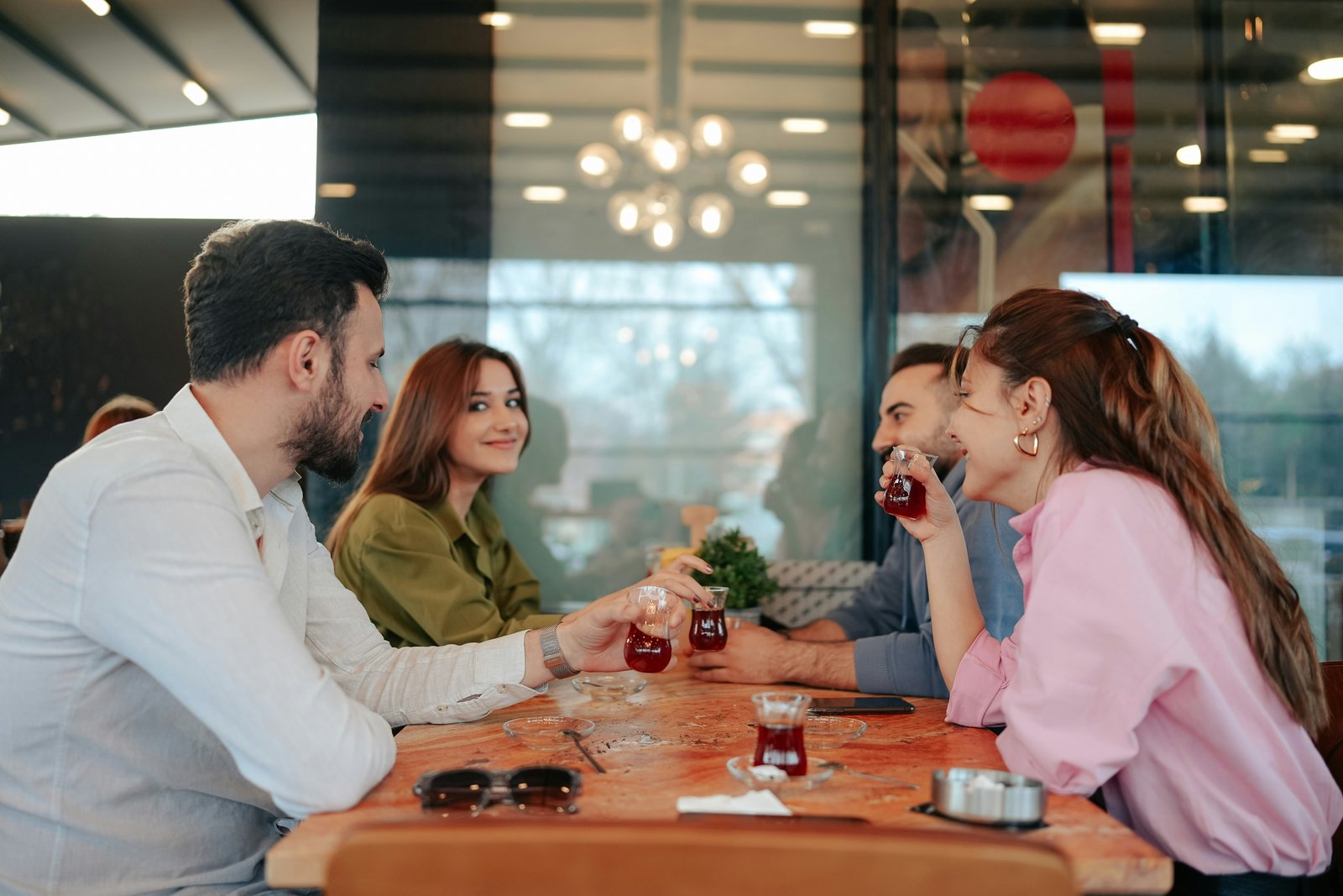 Four adults at a cafe table laughing together over drinks.