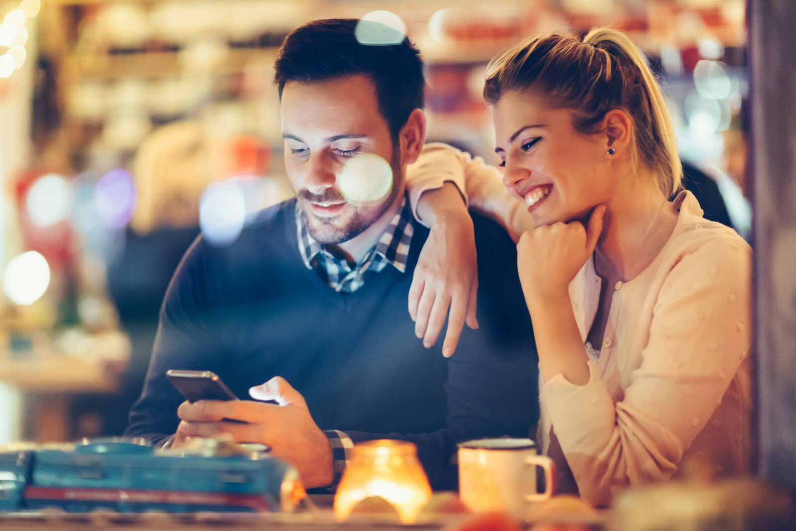 A couple sitting close together at a cafe, looking at a phone.